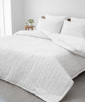 White textured comforter on a bed with pillows in a bright room.