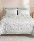 Bed with light gray floral patterned comforter and pillows in a bedroom setting.