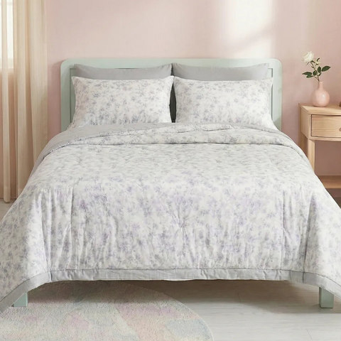 Bed with light gray floral patterned comforter and pillows in a bedroom setting.