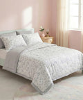 Bedroom with a bed featuring a floral comforter and pillows, a nightstand with a lamp and vase.