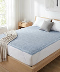 Bed with light blue geometric patterned mattress pad, gray pillow, and beige blanket in a bright bedroom.