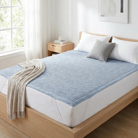 Bed with light blue geometric patterned mattress pad, gray pillow, and beige blanket in a bright bedroom.