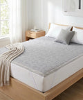Bed with gray geometric patterned mattress pad and beige throw in a bright bedroom