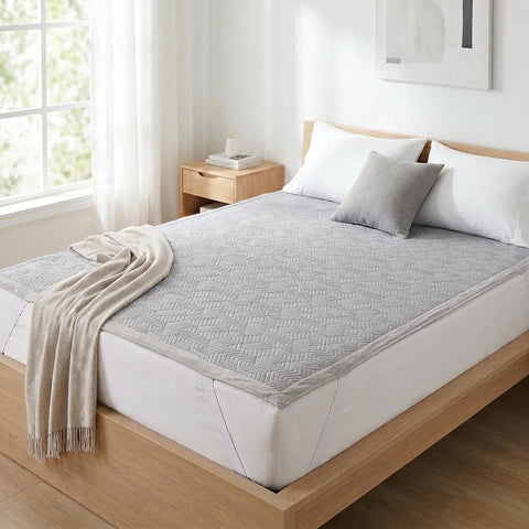 Bed with gray geometric patterned mattress pad and beige throw in a bright bedroom