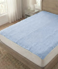 Blue mattress cover on a bed in a room with a window and side table.