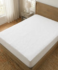 White mattress cover on a wooden bed in a bedroom with natural light.
