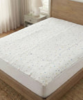 White mattress pad with small colorful dots on a wooden bed in a bedroom setting.