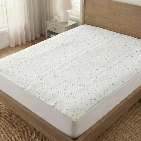 White mattress pad with small colorful dots on a wooden bed in a bedroom setting.