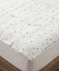 White quilted mattress cover with colorful speckles on a bed.