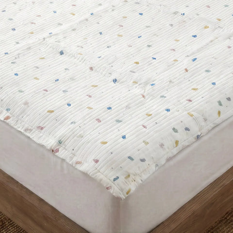 White quilted mattress cover with colorful speckles on a bed.