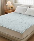 Light blue mattress cover on a bed in a bedroom setting with a lamp and plant on a nightstand.