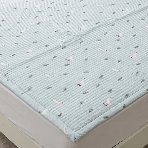 Quilted mattress cover with bird pattern on a bed