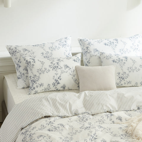 Floral and striped bedding set on a bed with white walls.