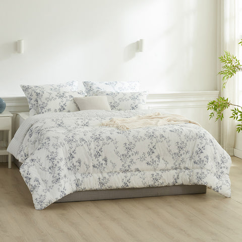Floral patterned comforter set on a bed in a bright bedroom with light wood flooring.