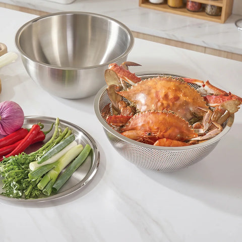 Stainless steel colander with cooked crabs on a kitchen counter with vegetables.