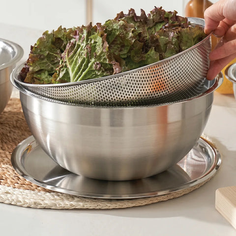 Stainless steel colander with lettuce being drained over a bowl on a kitchen counter.