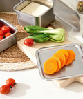 Stainless steel containers with sliced carrots and vegetables on a kitchen counter