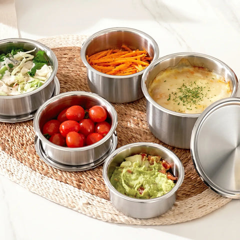 Set of stainless steel containers with various food items on a woven mat