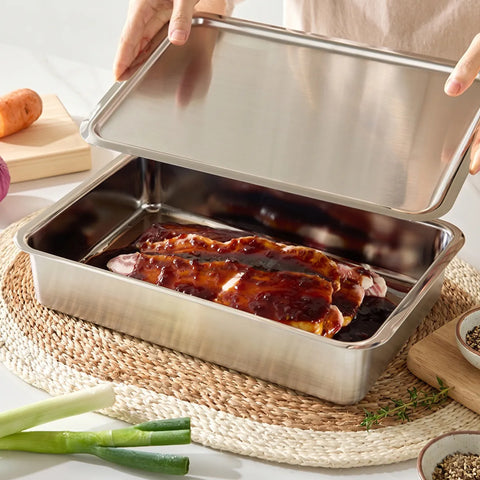 Stainless steel roasting pan with roasted meat on a woven mat, surrounded by vegetables.