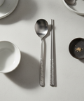 Silver spoon and chopsticks on a light gray surface with small dishes.