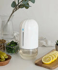 White humidifier on a table with lemons, pickles, and a plant in the background