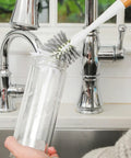 Person cleaning a glass with a brush under a faucet in a kitchen setting