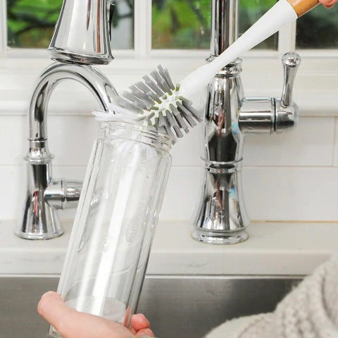 Person cleaning a glass with a brush under a faucet in a kitchen setting