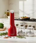 Red pepper grinder with two clear grinding chambers on a kitchen counter.