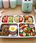 Stainless steel bento box with compartments of food on a wooden table.