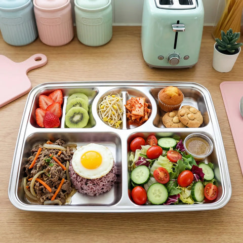 Stainless steel bento box with compartments of food on a wooden table.