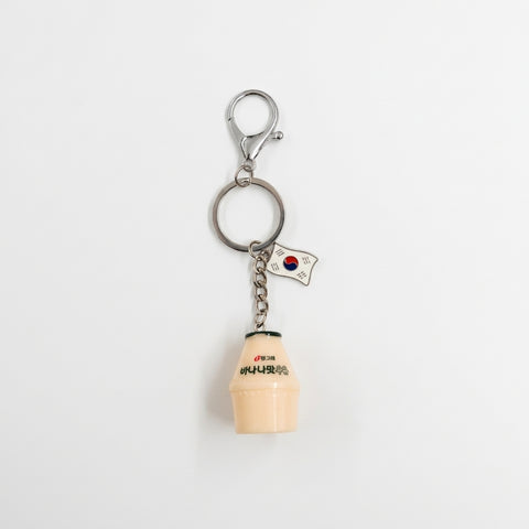A novelty keychain featuring a miniature beige plastic bottle with black Korean text, a small South Korean flag charm, and a silver metal lobster clasp on a white background.