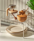 Kitchen setup with glass carafe, wooden containers, and plates on a metal rack.