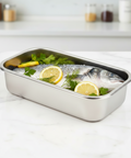 Stainless steel container with raw fish and lemon slices on a white surface