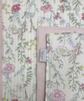 A close-up of a quilted fabric with a delicate pastel floral print on a cream background, featuring pink, green, and yellow flowers with a pink stitched border. A small fabric tag reading 'Casa Lux' is visible.