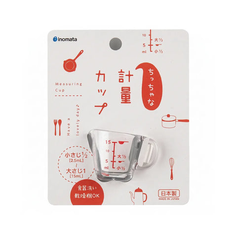 Anomata measuring cup in its original retail packaging, featuring a clear glass measuring cup with red measurement markings on a white card with red and black illustrations.