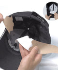 Person applying a white hat protector strip on the inside of a black cap on a white background.