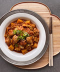 Stir-fry dish with vegetables and meat on a white plate with chopsticks on a wooden board.