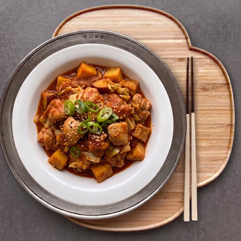 Stir-fry dish with vegetables and meat on a white plate with chopsticks on a wooden board.