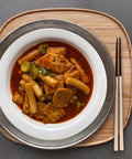 Stir-fried dish with Korean tteokbokki on a white plate with chopsticks on a wooden tray.