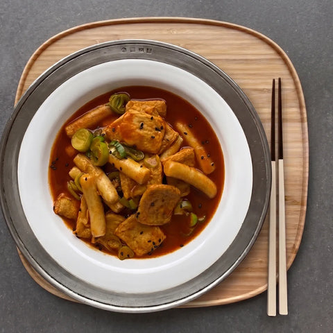 Stir-fried dish with Korean tteokbokki on a white plate with chopsticks on a wooden tray.