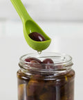 Green scoop taking an olive from a jar on a white background