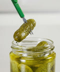 Jar of pickles with a green pickling fork lifting a pickle out.