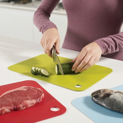 Person cutting vegetables on a green cutting board with other food items on colorful boards.