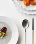 Two plates with food, a spoon, and chopsticks on a white surface