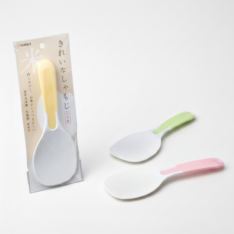 Three plastic rice spoons with textured white heads and pastel handles are shown beside their retail packaging. One handle is pale yellow and the other is pale green and pink.