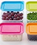 Set of colorful food storage containers with lids containing grapes, peas, rice, and black beans.