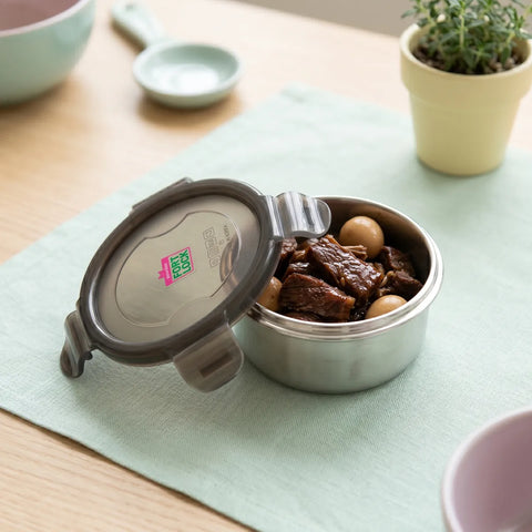 Stainless steel food container with food on a table with a plant in the background