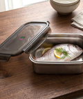 Stainless steel container with fish and lemon on a wooden table