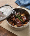Stainless steel food container with beef stew on a wooden table