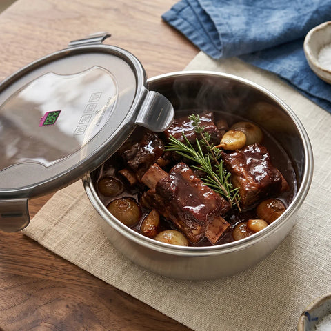 Stainless steel food container with beef stew on a wooden table